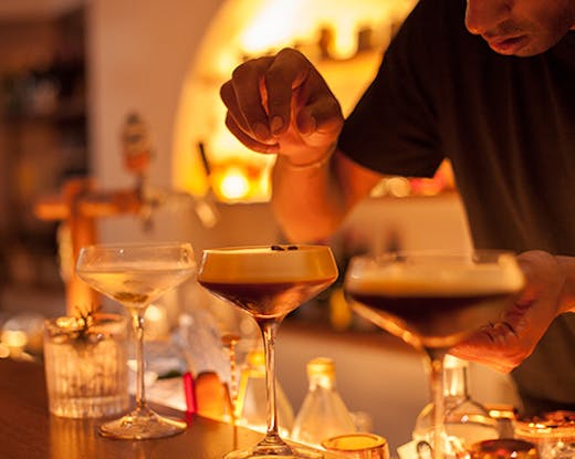 A bartender sprinkles coffee beans on a row of espresso martinis.