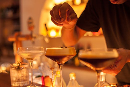 A bartender sprinkles coffee beans on a row of espresso martinis.