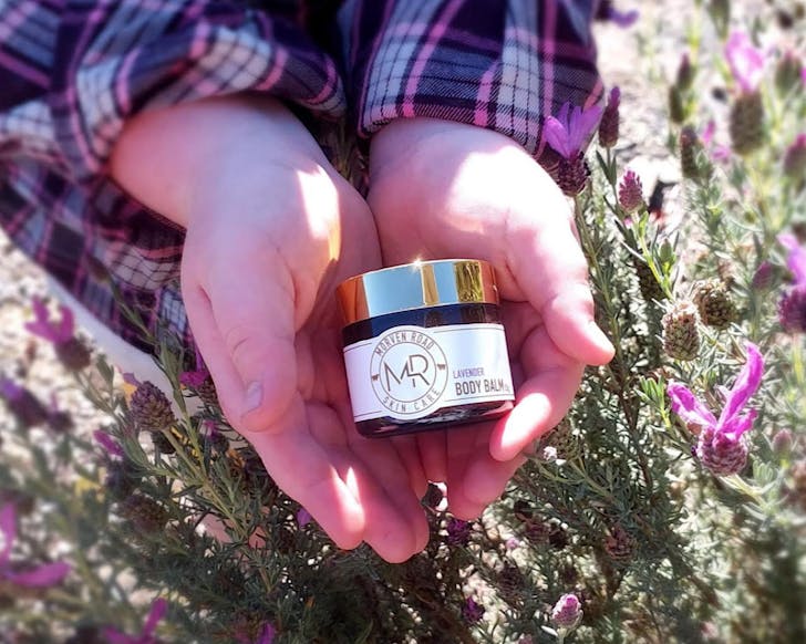 Hands holding a pot of body balm.