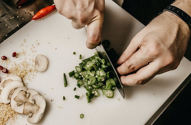 A person chopping up jalapenos on a chopping board.