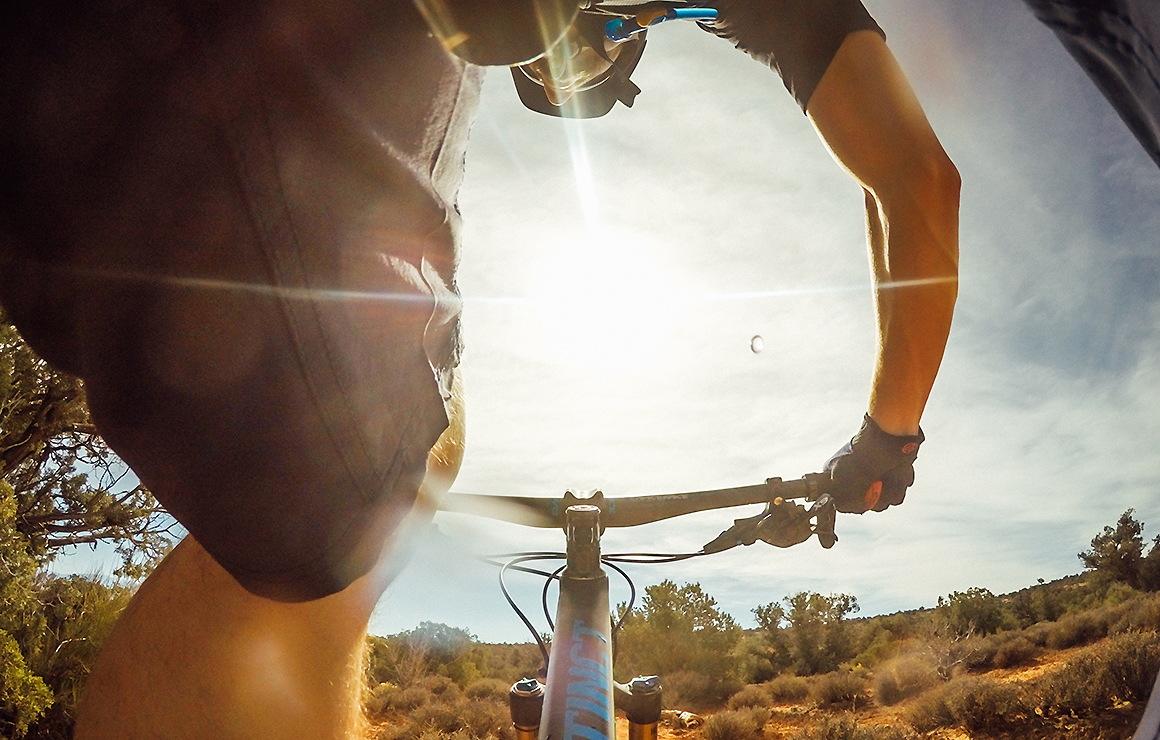 A man rides a mountain bike over rough terrain, we only see the sun and the cross bar.