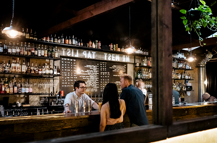 A shelf lined with bottles and a bartender at one of the best bars in Melbourne.