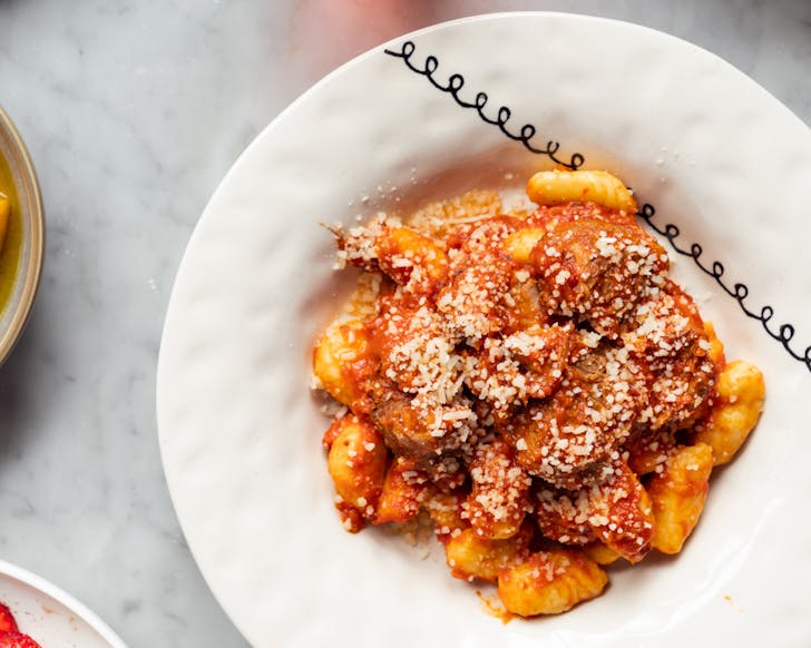 a bowl of gnocci with red sauce on a white tablecloth