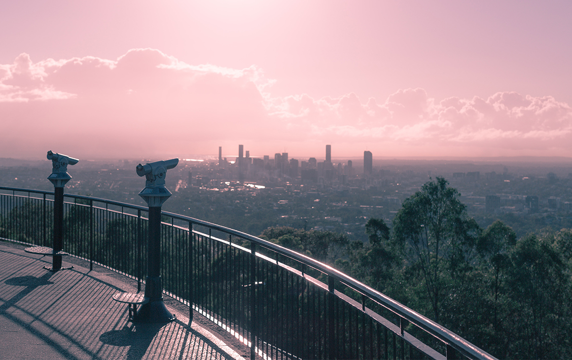The view from the top of Mt Coot-tha, with Brisbane CBD in the distance and a pink sunset colouring the image