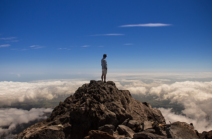 A man stands atop Mount Taranaki looking at nothing but sky.