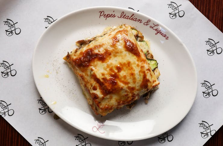 A slice of mushroom lasagne on a plate that says Pepe's Italian & Liquor.