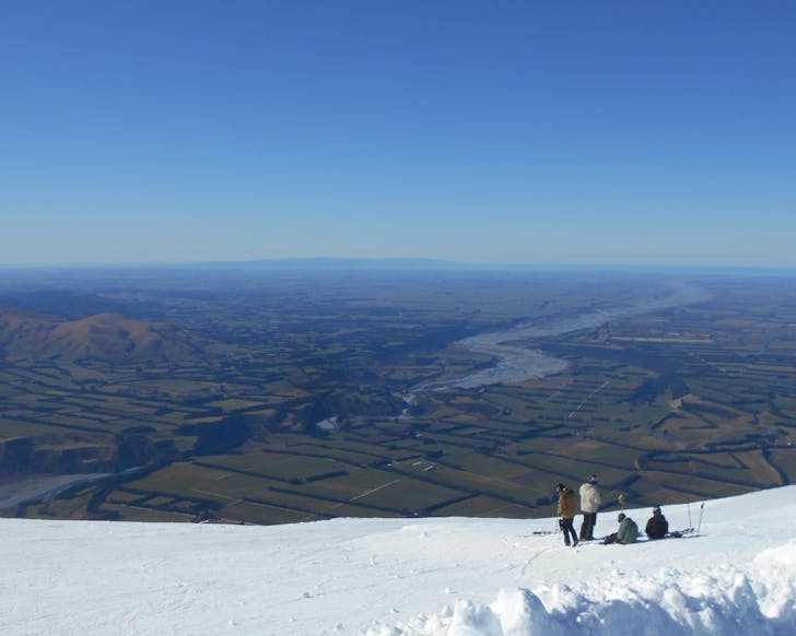 A group of skiers slightly off piste gaze out from Mt Hutt across the Canterburian plains on a crisp, clear bluebird day.