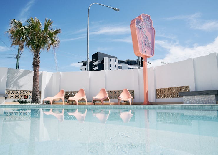 the exterior of a retro motel with kidney shaped pool and a neon pink sign and a palm tree