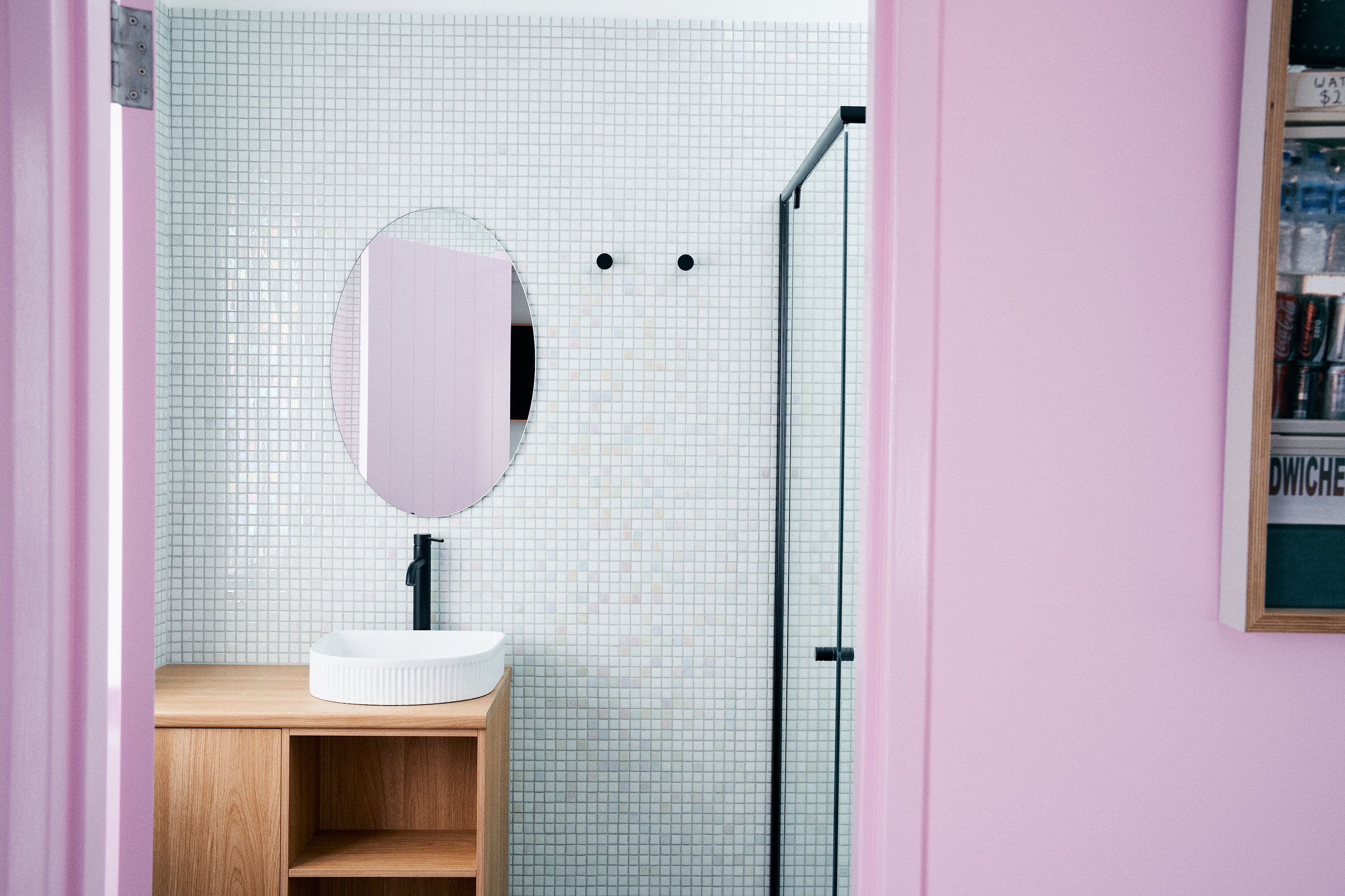 a pink bathroom with white tile and an oval mirror