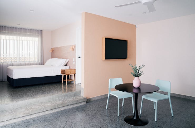 a motel room with a small table with turqoise chairs and a salmon pink wall and a tv