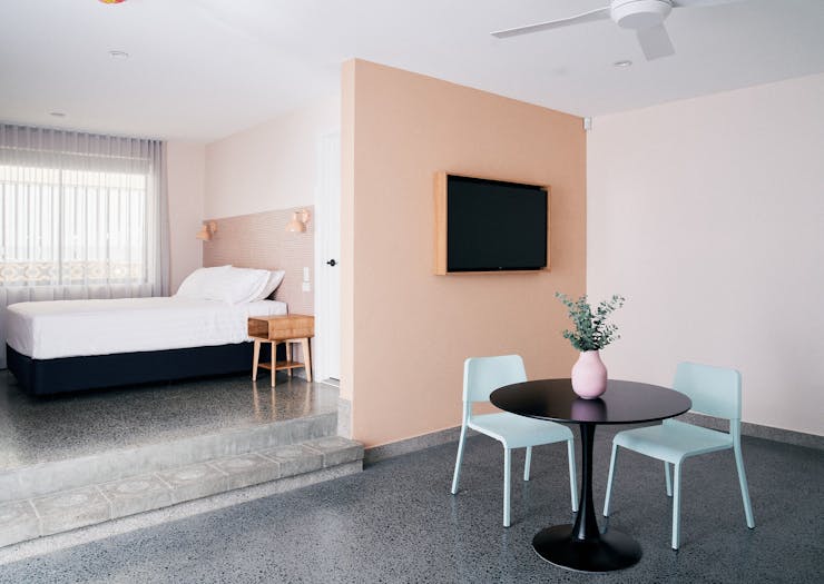 a motel room with a small table with turqoise chairs and a salmon pink wall and a tv