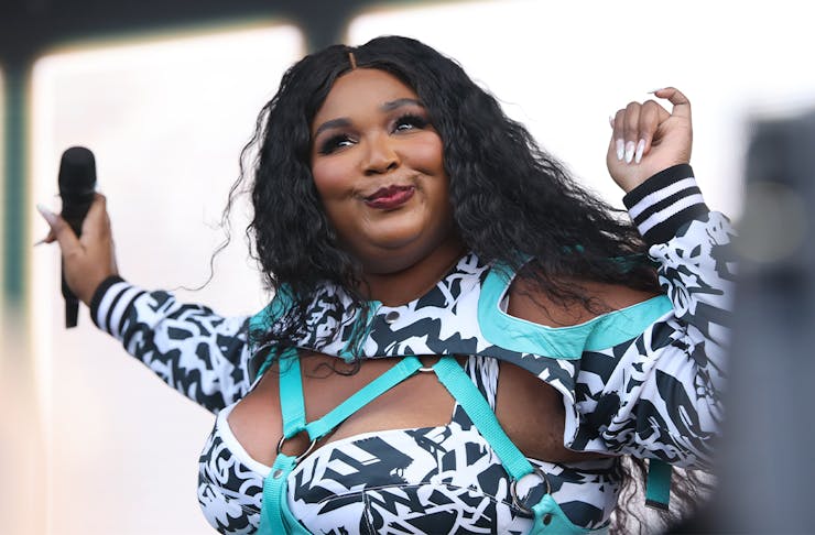 Lizzo singing on stage in a bright blue geometric outfit with long french tip nails.