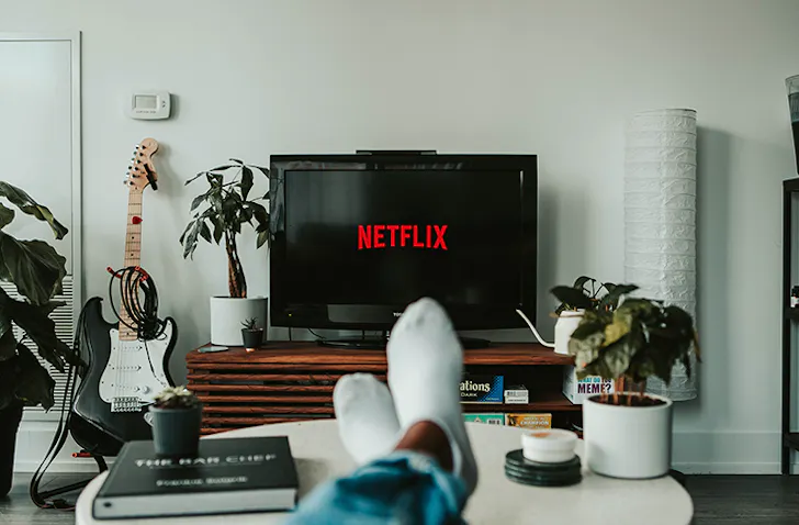 Person sitting on couch in blue jeans, watching Netflix on TV.