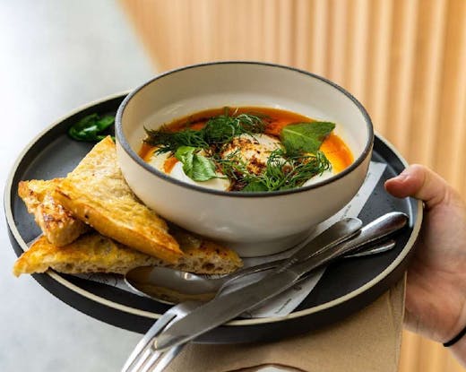 Plate with toasted turkish bread, accompanied with a bowl of Turkish eggs and cutlery