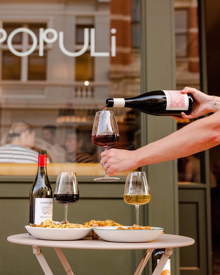 A glass of red being poured at the table alongside bowls of pasta at Vin Populi