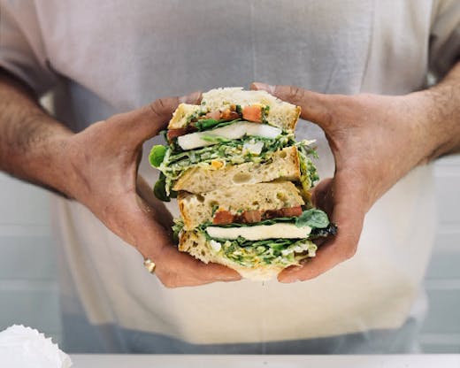 A stacked deli sandwhich being held in two hands from Nico's Sandwich Deli.