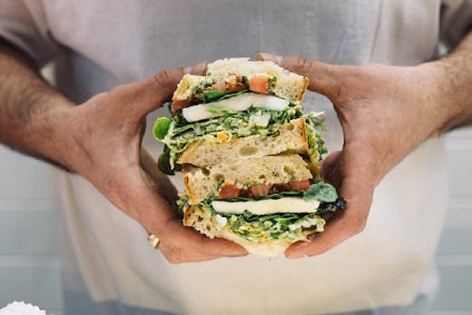A stacked deli sandwhich being held in two hands from Nico's Sandwich Deli.