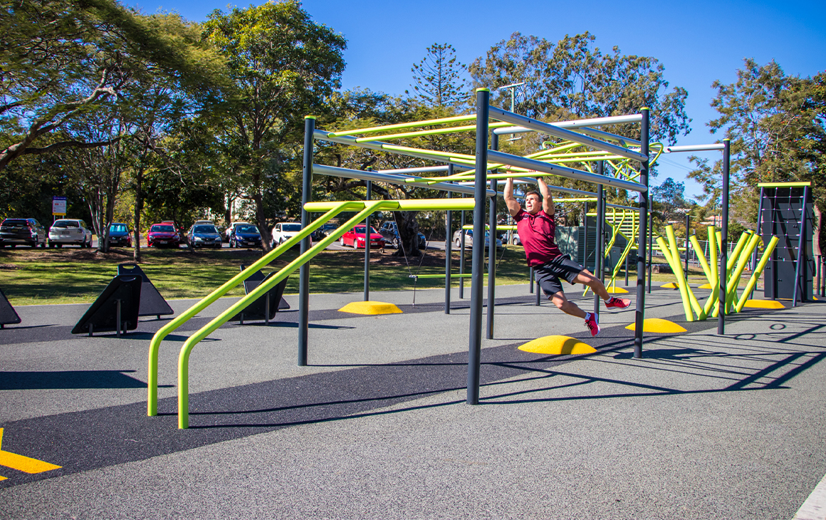 A man hanging from a set of bars in a park