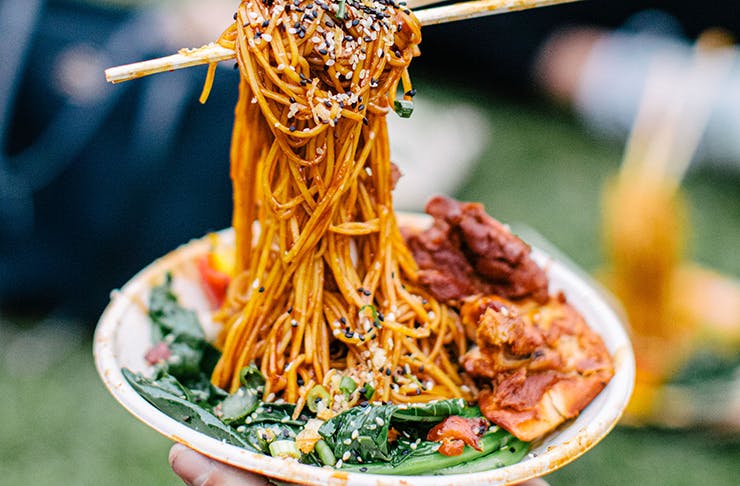 Chopsticks in a bowl of noodles with various trimmings on top.