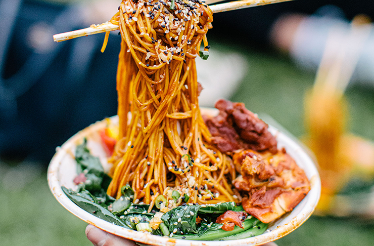 Chopsticks in a bowl of noodles with various trimmings on top.