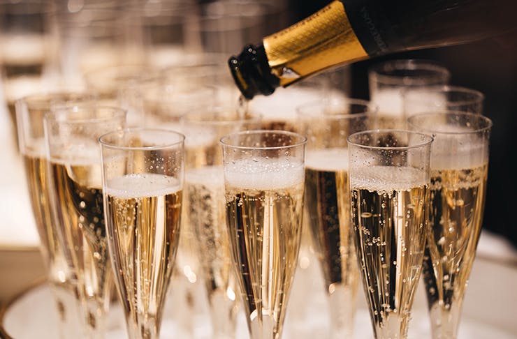 A champagne bottle filling up champagne glasses.
