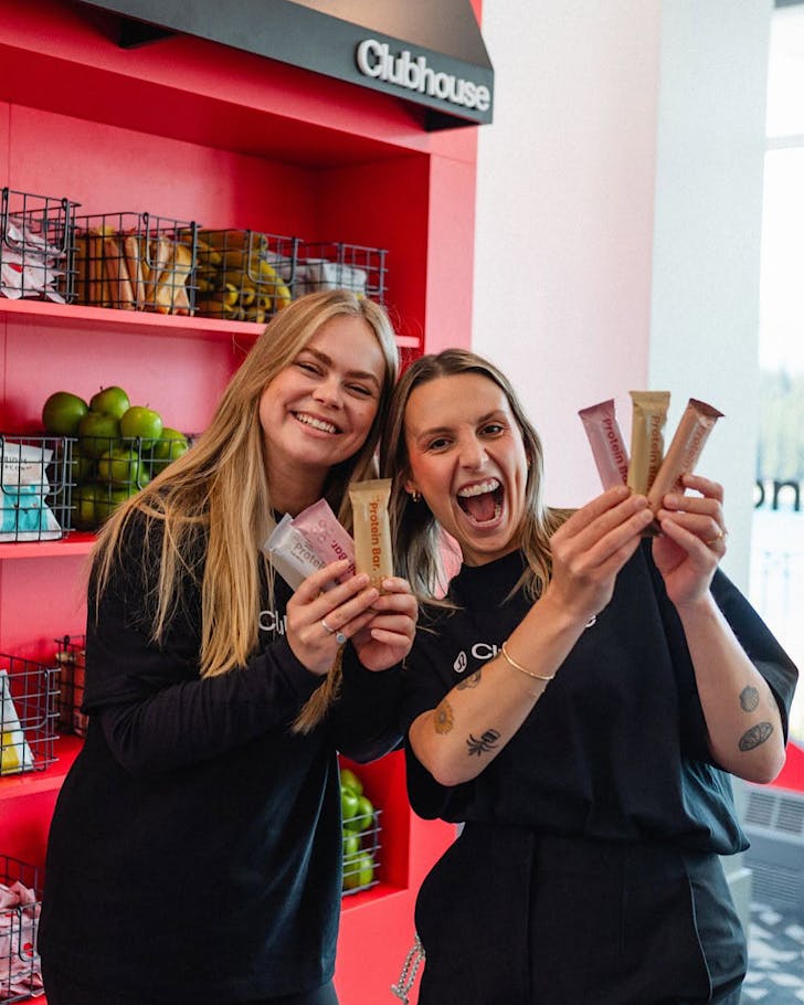 Two people hold up Nothing Naughty protein bars in the brightly coloured Nothing Naughty store.
