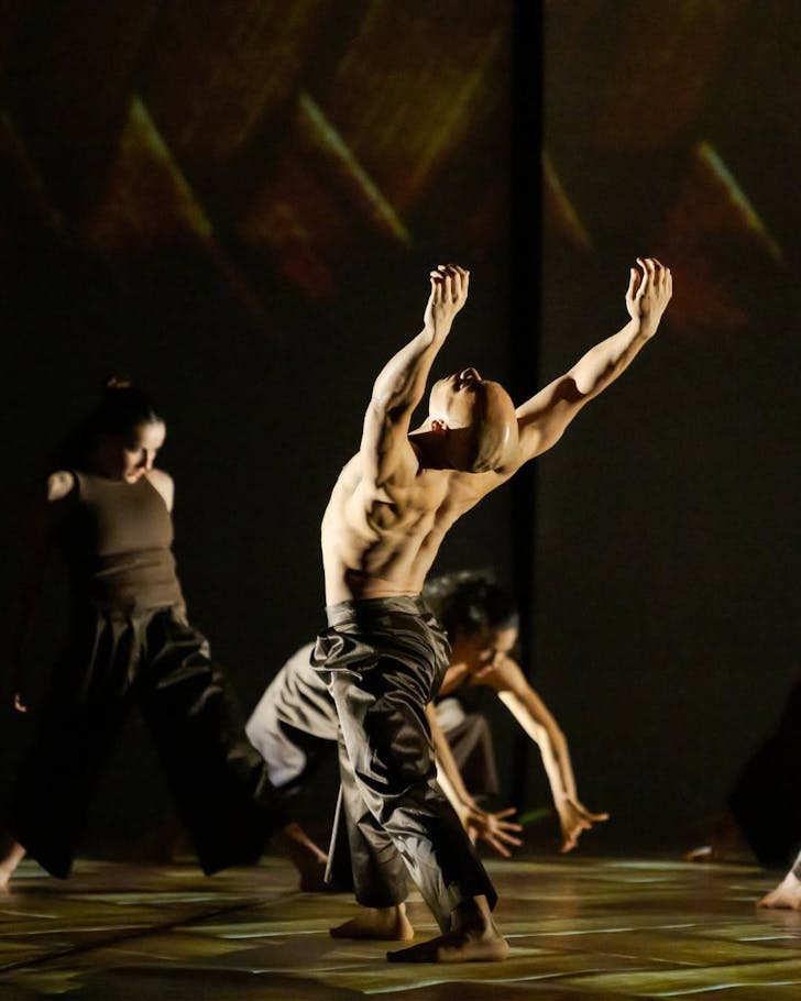 A Home, Land & Sea performer thrusts their hands in the air, muscles rippling.
