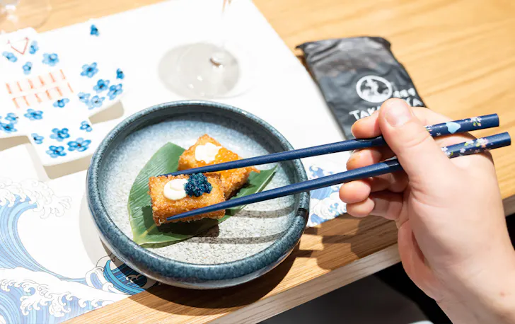 a person's hand using chopsticks to pick up a morsel of food