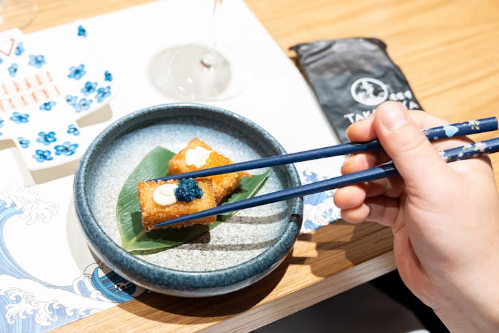 a person's hand using chopsticks to pick up a morsel of food