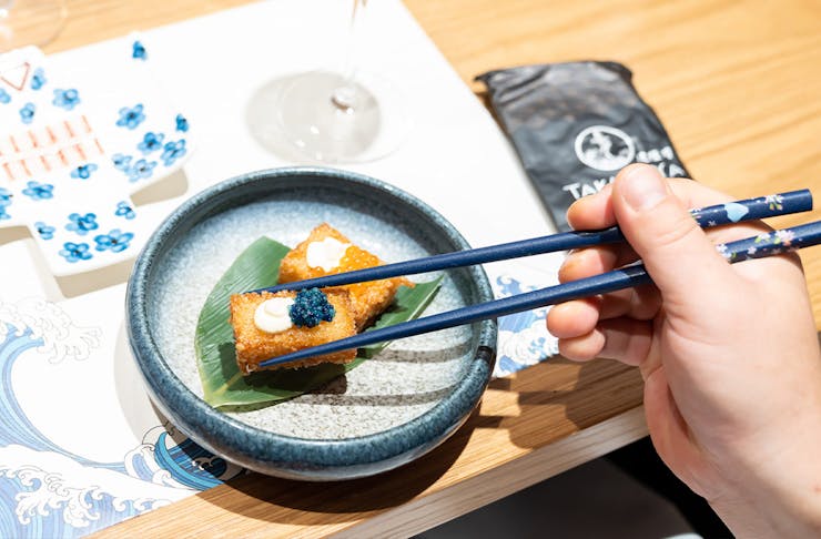 a person's hand using chopsticks to pick up a morsel of food