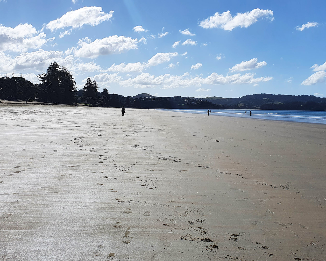 Footprints on a white sand beach with several figures in the background. 