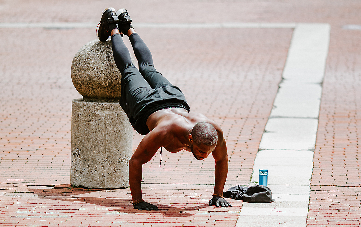 A man does push ups with his feet unfeasibly high on an outdoor sculpture. He looks very fit. 