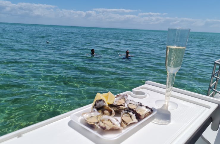 A tray of oysters and glass of champagne on a boat overlooking clear blue water.