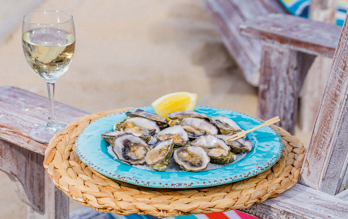 half a dozen oysters on a plate on the arm of a wooden chair with a glass of wine