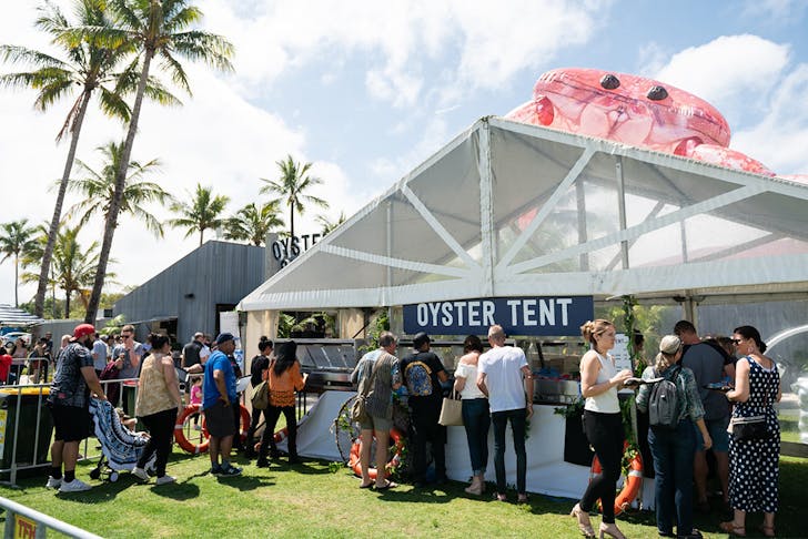 a large white tent that says 'oyster tent' with a queue of people outside it