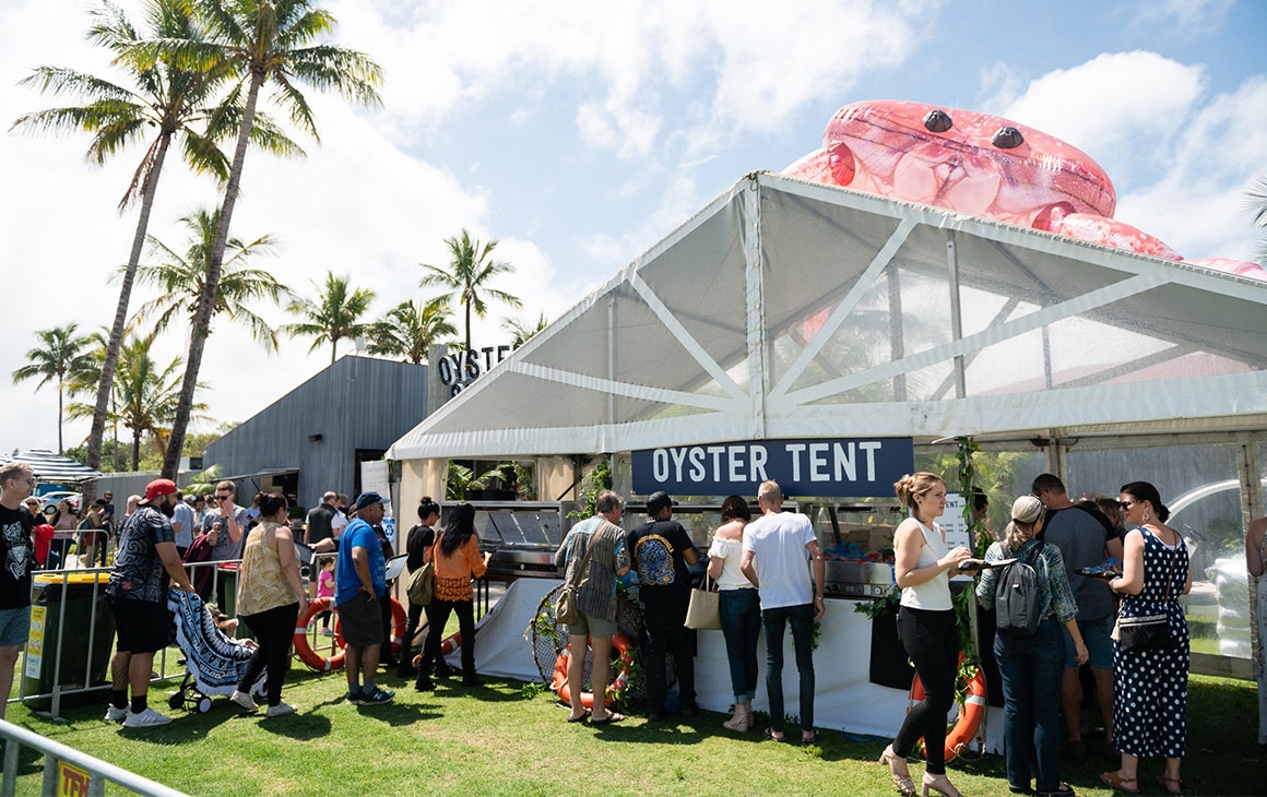 a large white tent that says 'oyster tent' with a queue of people outside it