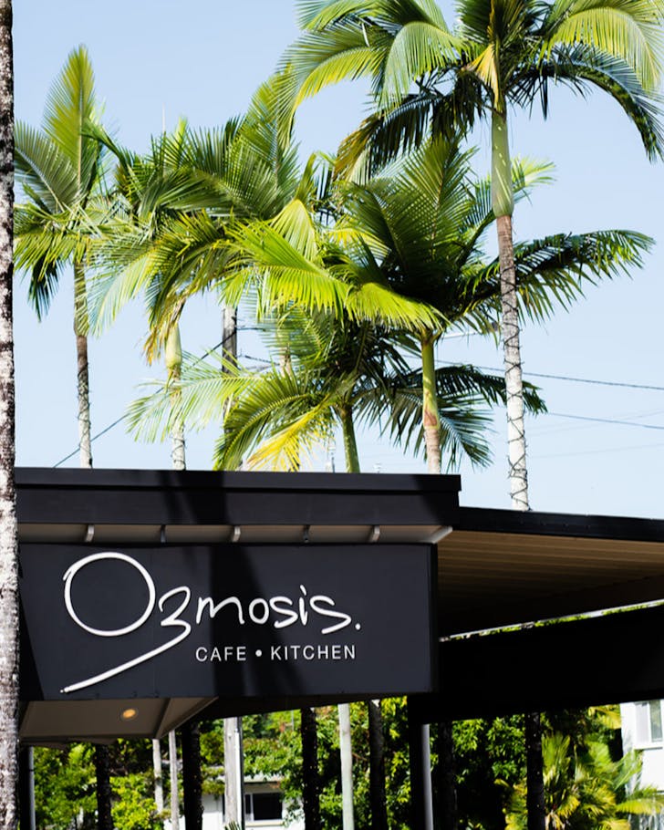 The sign for Ozmosis in Cairns against a backdrop of tall palm trees.
