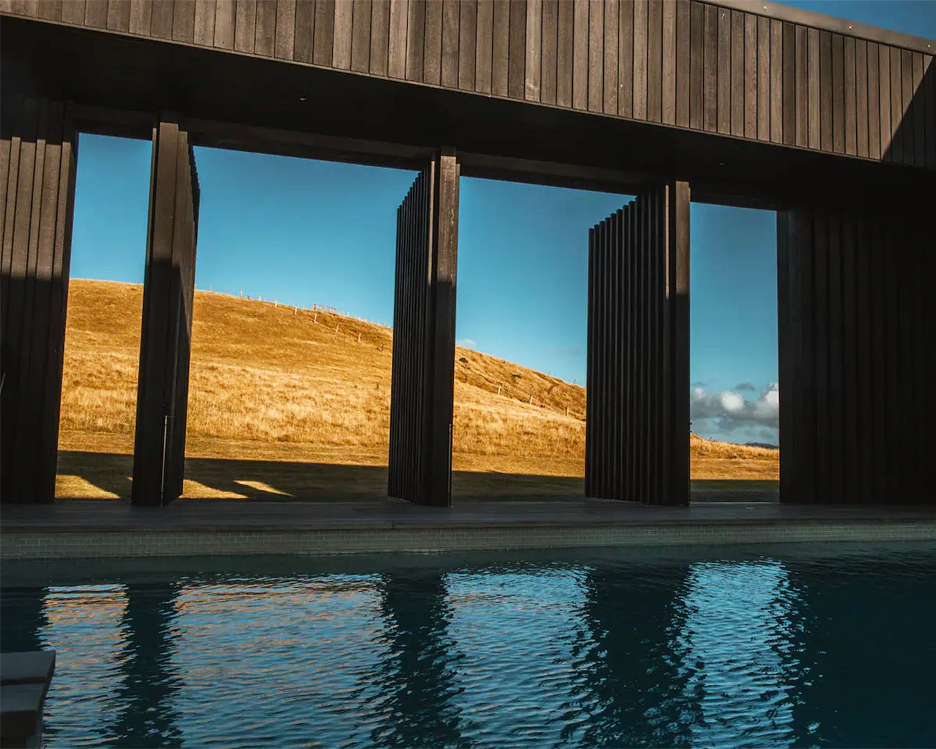 A gorgeous pool with doors that open up to a field and clear blue sky. 