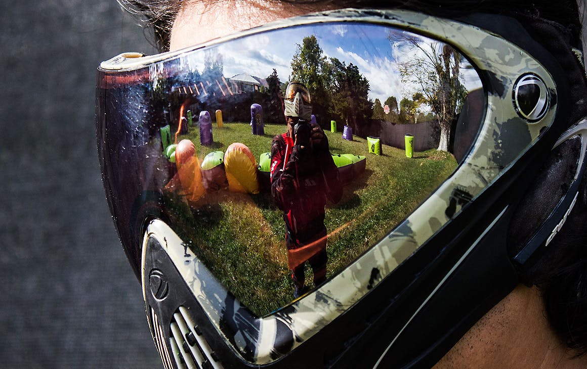 A man wearing a mask shows the reflection of another man taking aim.