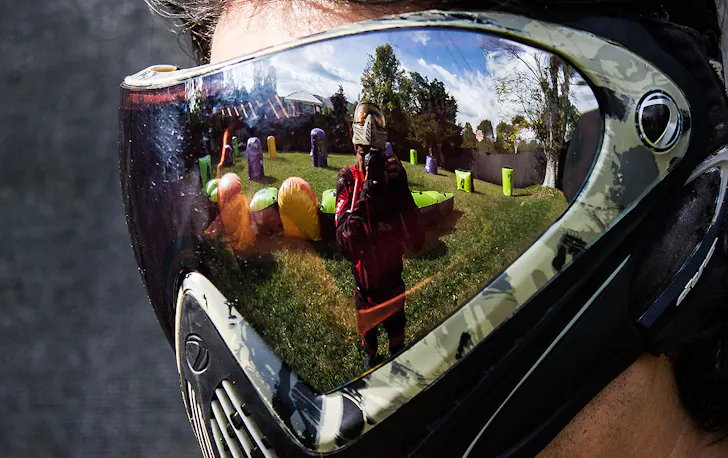 A man wearing a mask shows the reflection of another man taking aim.