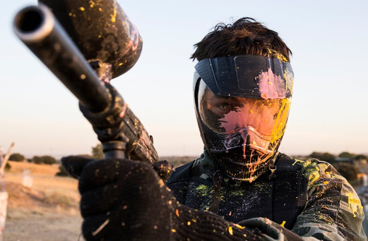 A man holding a paintball gun wearing a face shield