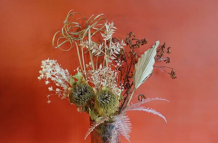 A dried flower arrangement in front of a red background.
