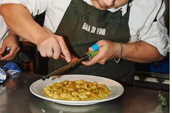 a chef grates parmesan over a bowl of pasta