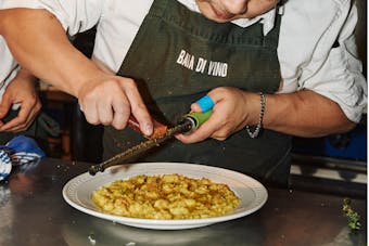 a chef grates parmesan over a bowl of pasta