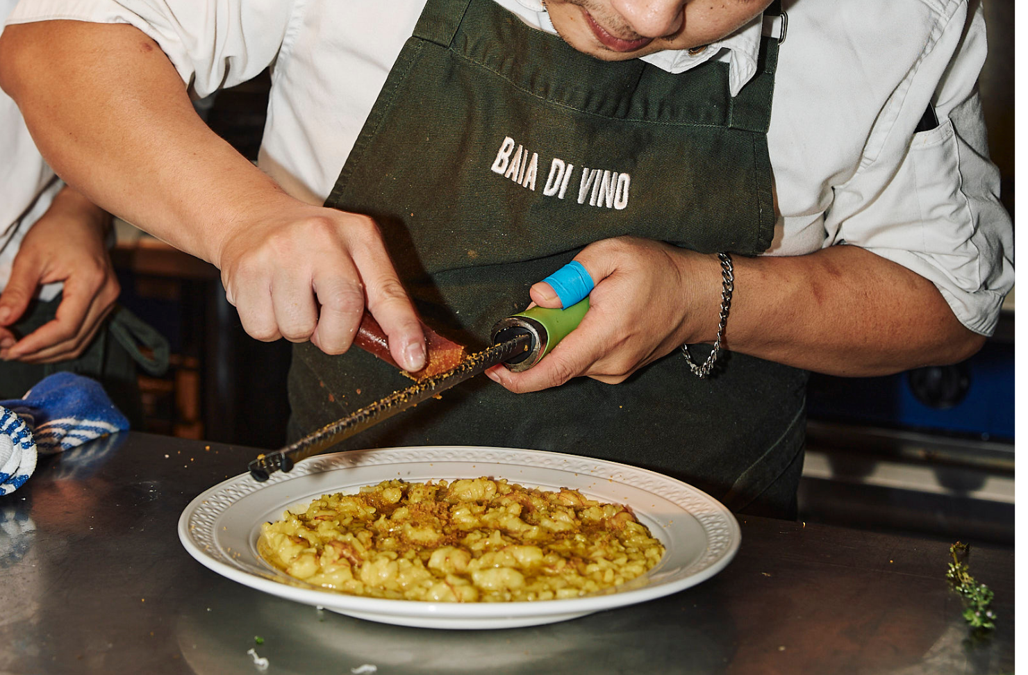 a chef grates parmesan over a bowl of pasta