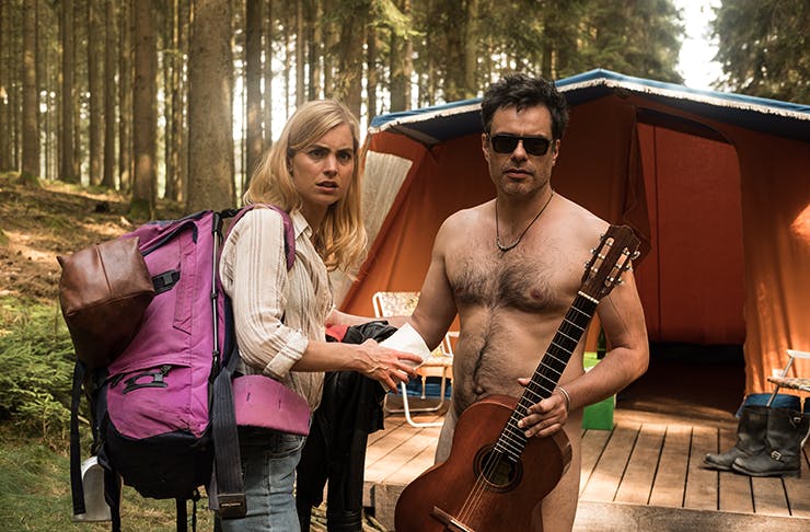 A naked man holding a guitar covering his crotch. 