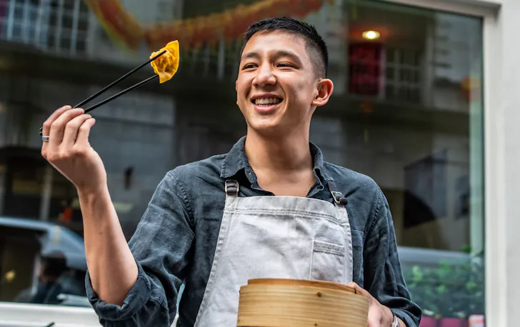 Brendan Pang holds up dumpling with chopsticks