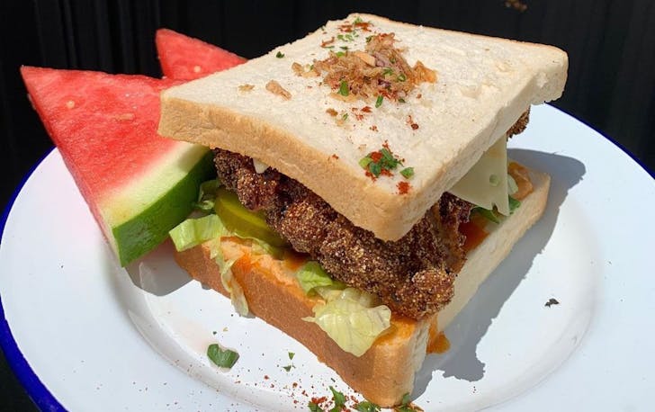 a buffalo fried chicken sandwich ona. white plate with slices of watermelon