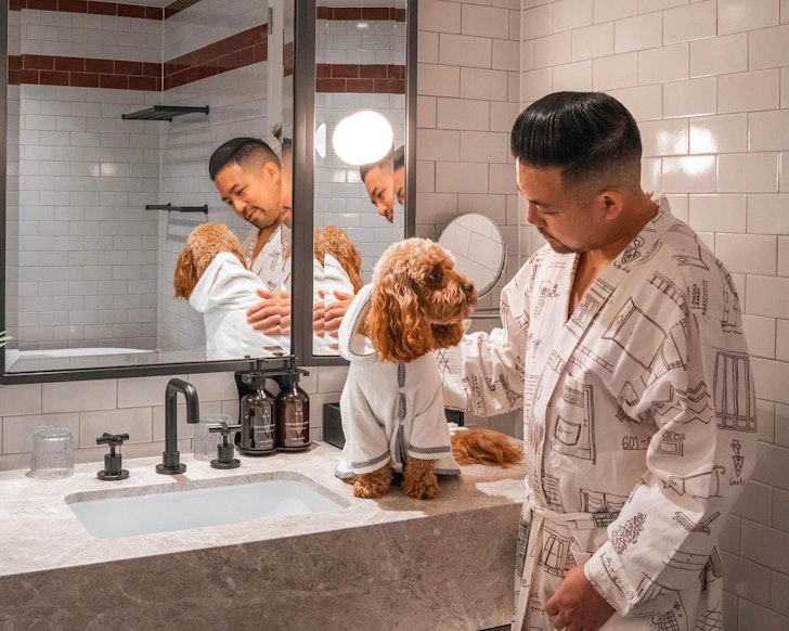 A man pats his dog in the bathroom of a room at Kimpton Margot pet-friendly hotel Sydney