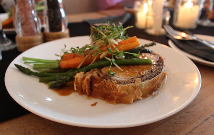 Colourful main dish of pork wrapped in flaky bread crust topped with asparagus, carrots and microgreens